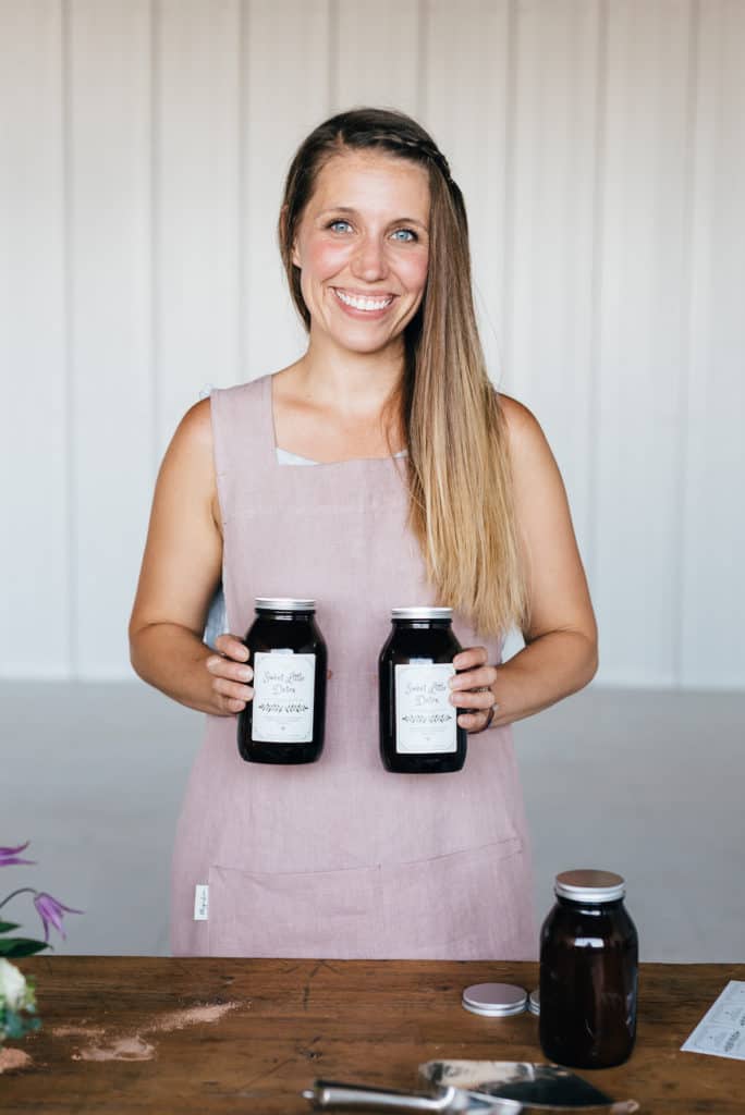 woman in an apron smiling holding two jars