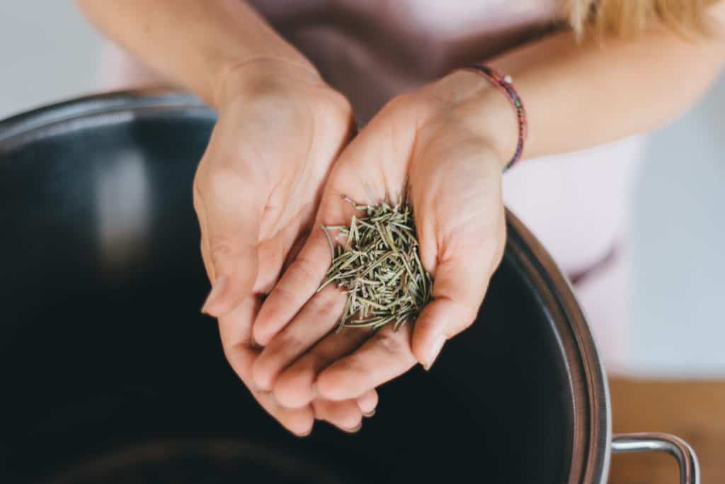 close up of hands hold herbs over a steel pot