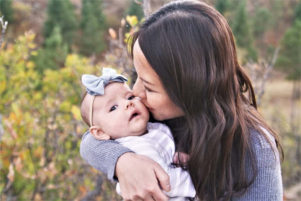 woman holding and kissing her infant on the cheek while outdoors