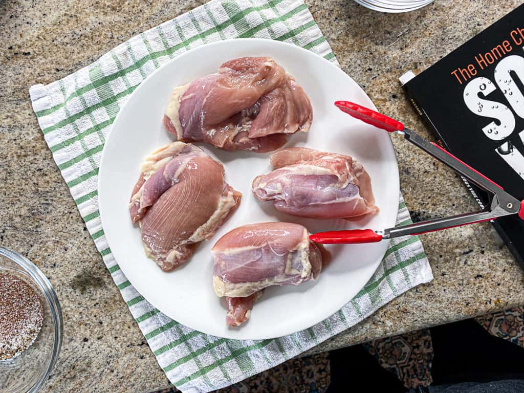 top shot of boneless chicken thighs on a plate with tongs