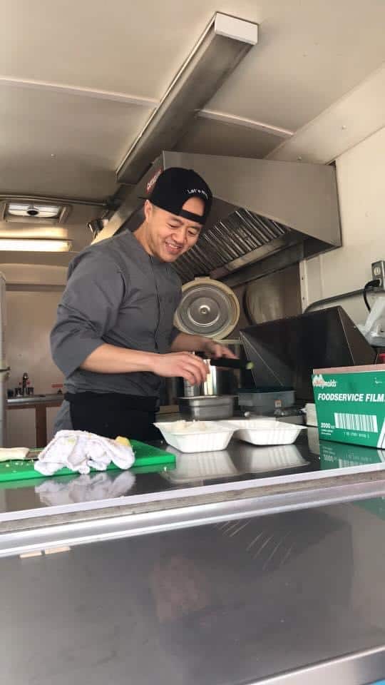 man in kitchen putting food into take out container and smiling