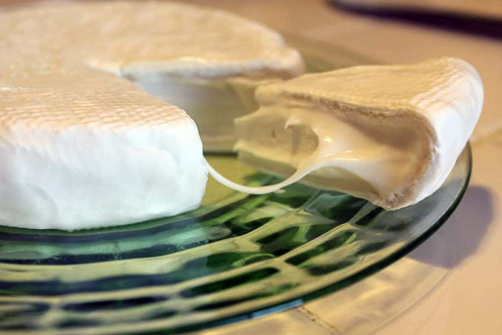 a round of brie cheese with a wedge cut cut and pulled out from the wheel, on green glass plate