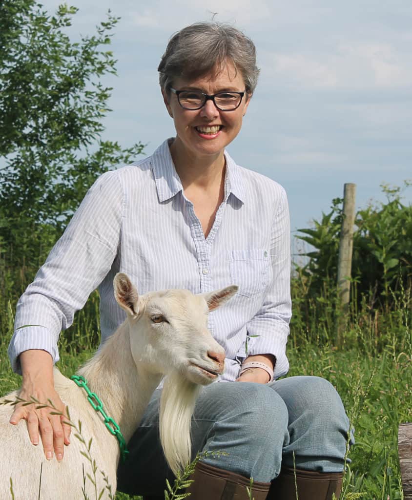 Woman smiling, sitting in greenery with a white goat