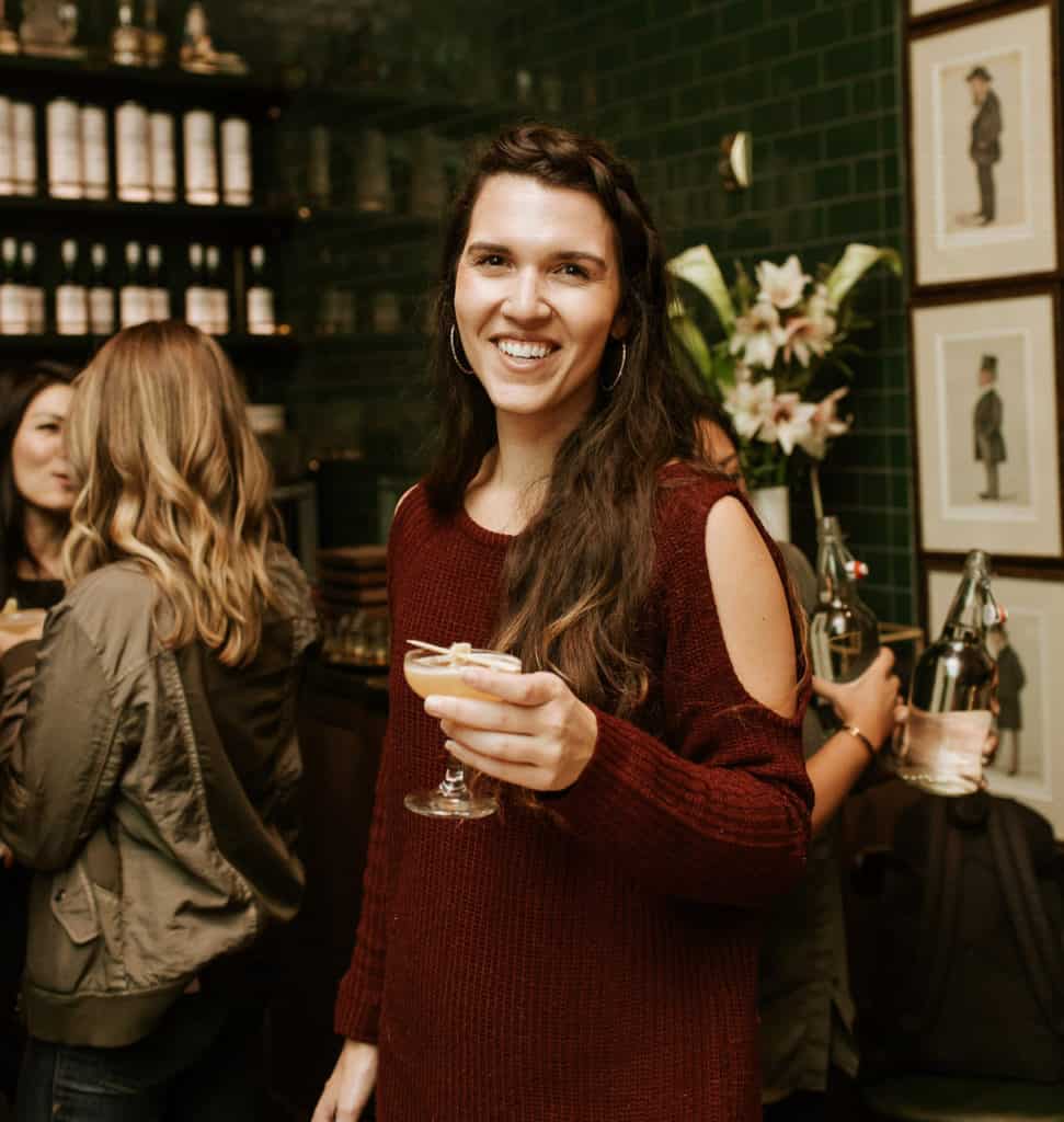 smiling woman in a red sweater holding a cocktail class in a restaurant