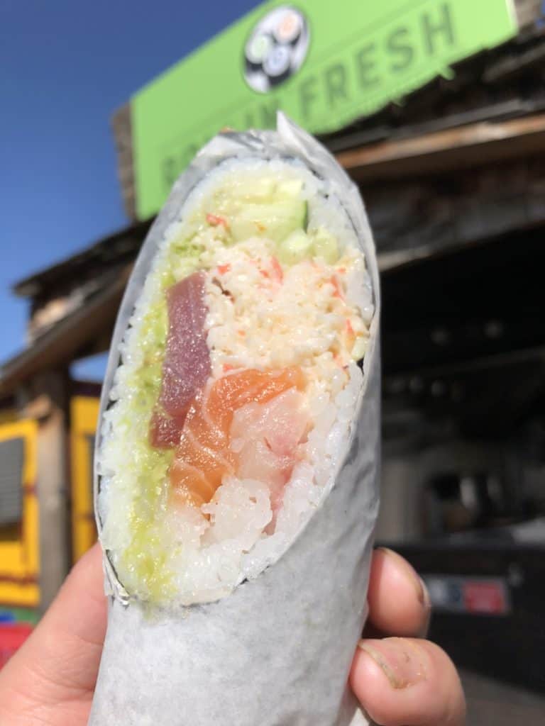 close up of sushi burrito with rollin fresh storefront in the background