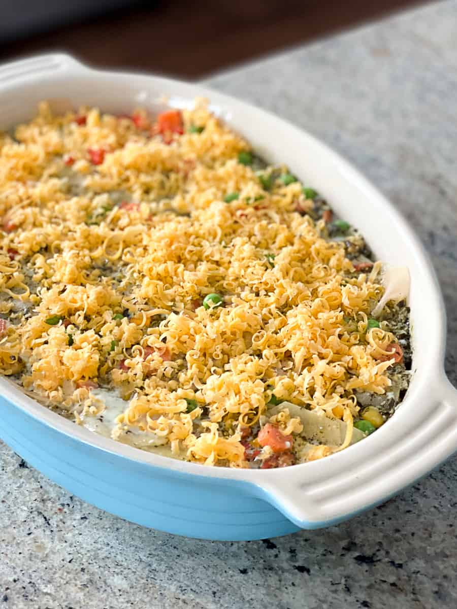 Frozen mixed vegetables potato au gratin topped with grated cheese in white casserole dish.