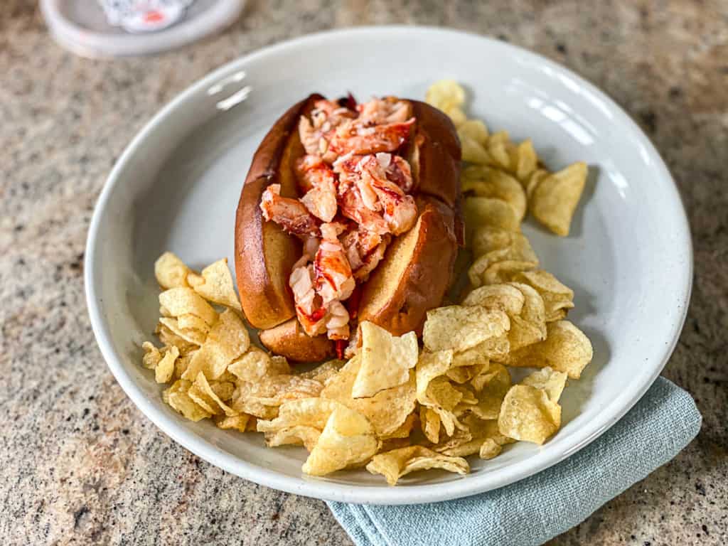 lobster roll with potato chips surrounding it on a plate