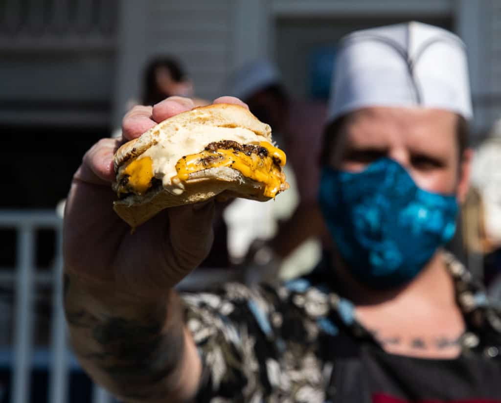 man in blue face mask holding a burger out in front of him