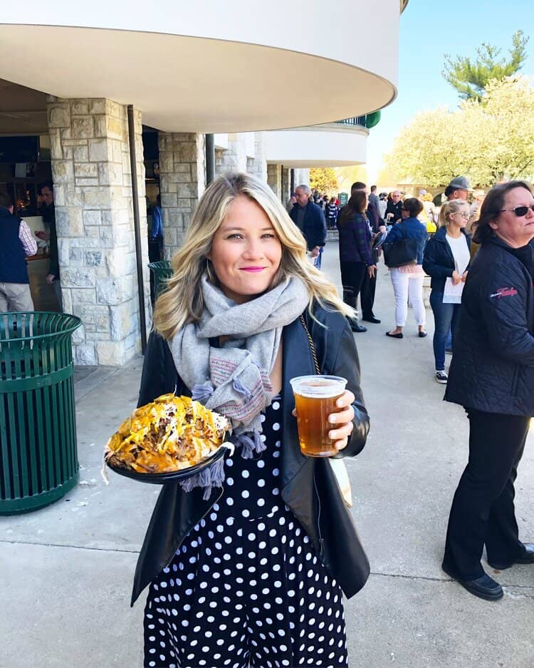 woman in a scarf smiling, holding nachos and a beer