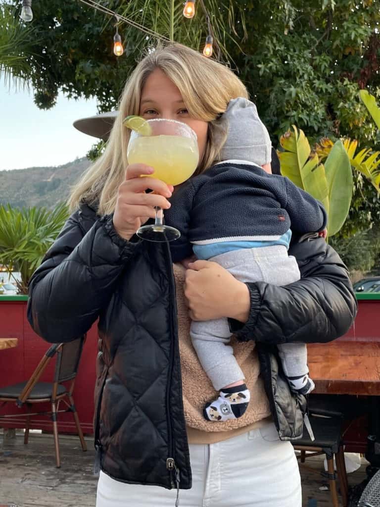 woman holding baby while drinking a margarita