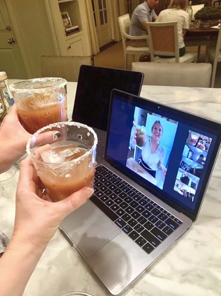 two people holding drinks toward a computer screen with a zoom happy hour on the laptop