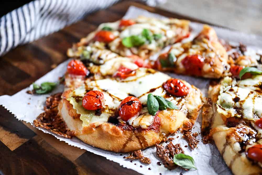Top shot ravioli pizza on flatbread, topped with mozzarella cheese and cherry tomatoes.