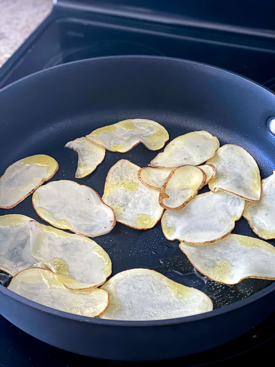Homemade potato chips cooking in black sauce pan on oven.