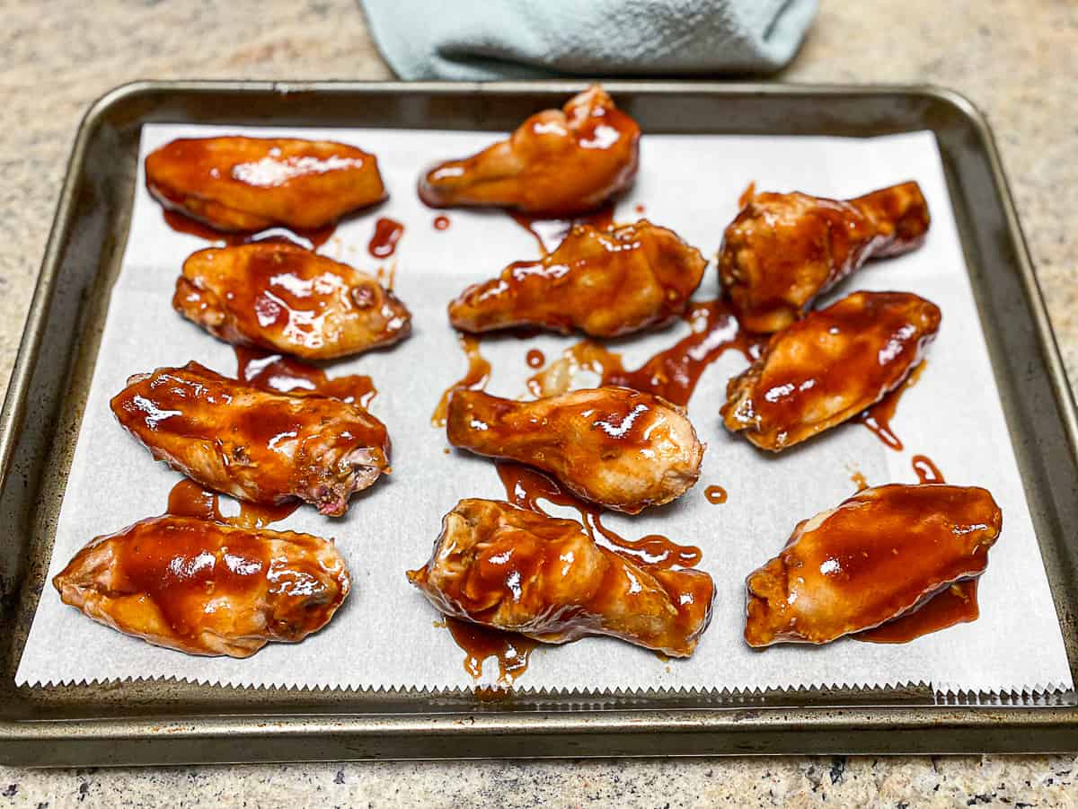 BBQ chicken wings on parchment paper on baking sheet covered in sauce.