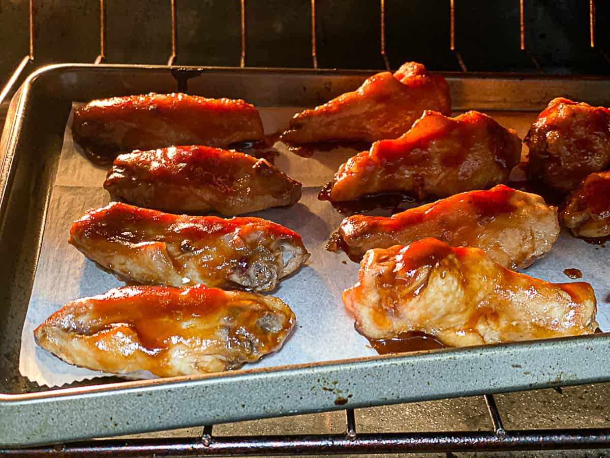 Chicken wings with BBQ sauce on baking sheet cooking in oven.