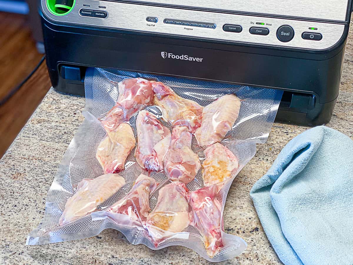 Uncooked chicken wings in plastic bag being vacuum sealed.