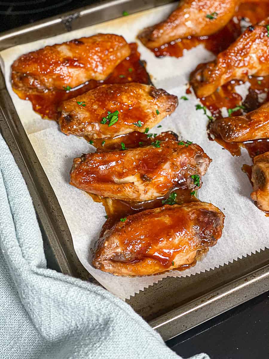 BBQ chicken wings on parchment paper on baking sheet covered in sauce.