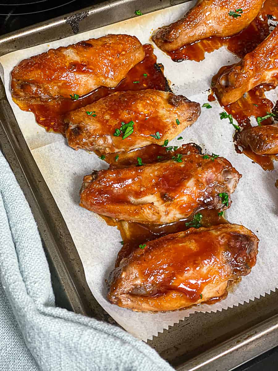 Chicken wings covered in sauce on parchment paper on baking sheet covered in sauce.