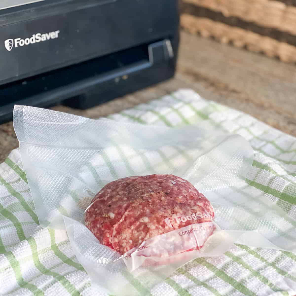 Uncooked lamb burger patty in vacuum sealed plastic bag on top of tea towel.