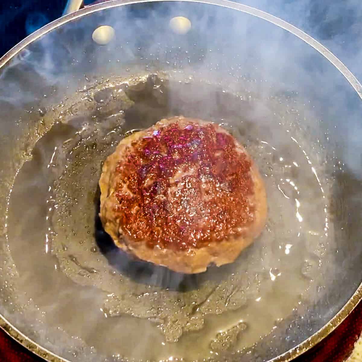 Meat patty cooking in skillet.