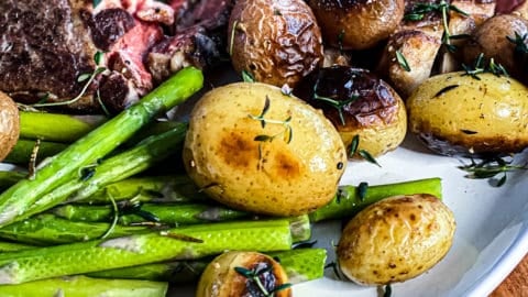 Close up shot of potatoes, asparagus, and steak on white plate.