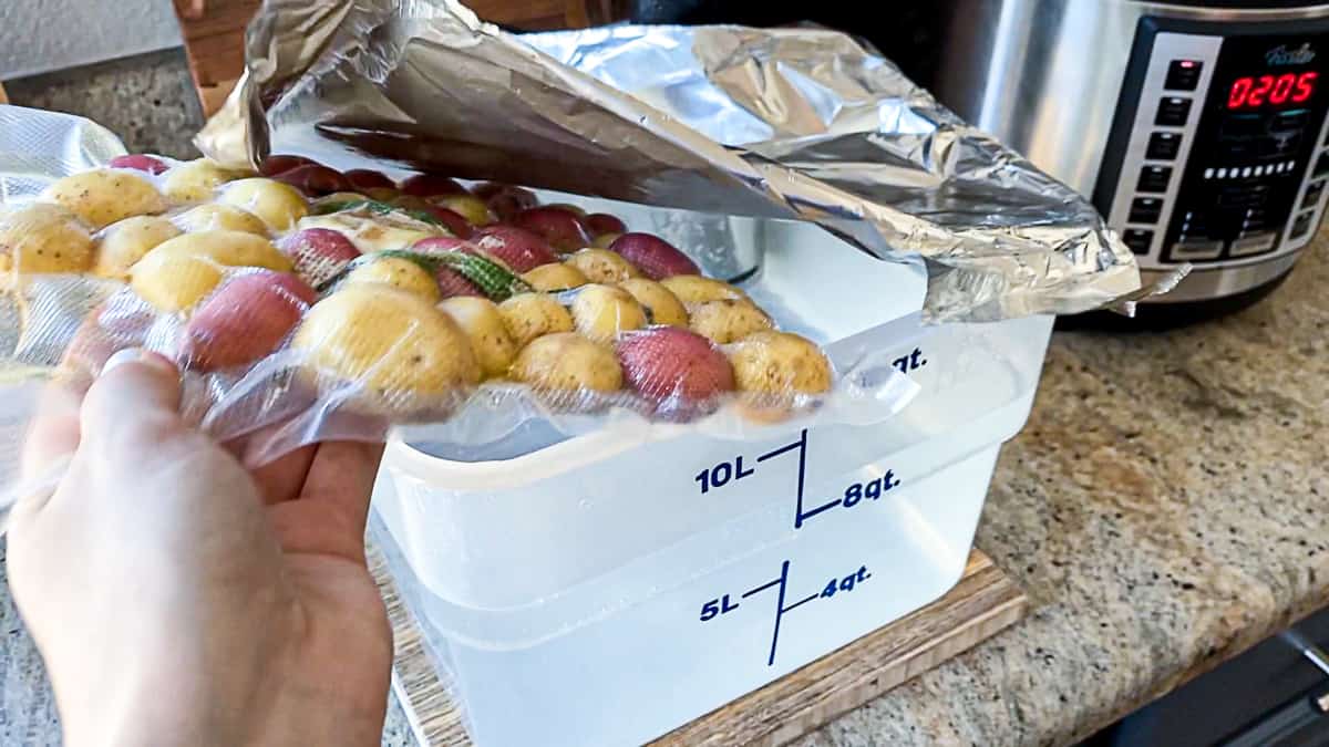 Small potatoes in vacuum sealed bag being placed in sous vide bucket of water, covered in tin foil.