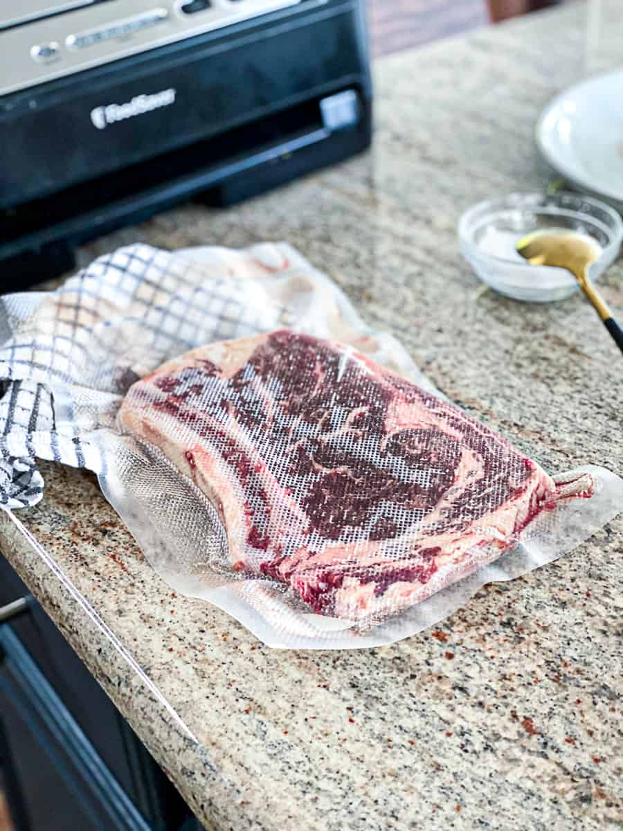 Ribeye steak in vacuum sealed plastic bag on countertop.
