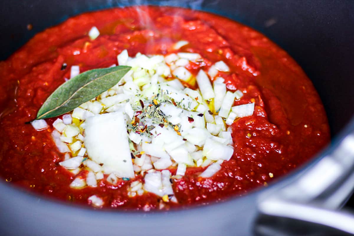 Side shot of tomato sauce cooking with bay leaf and onions in a pot.