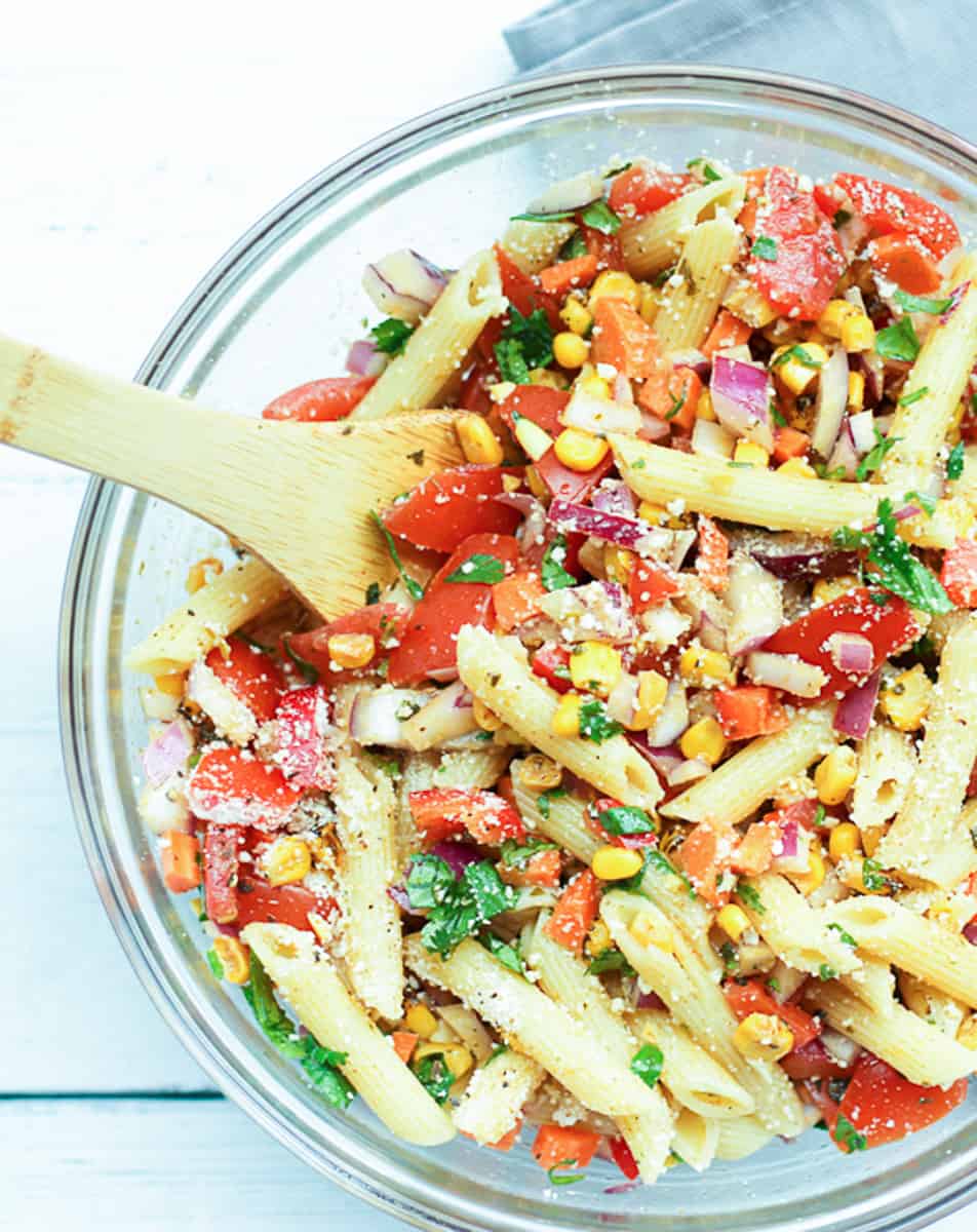 Top down shot of pasta salad with corn and tomatoes in a serving bowl.