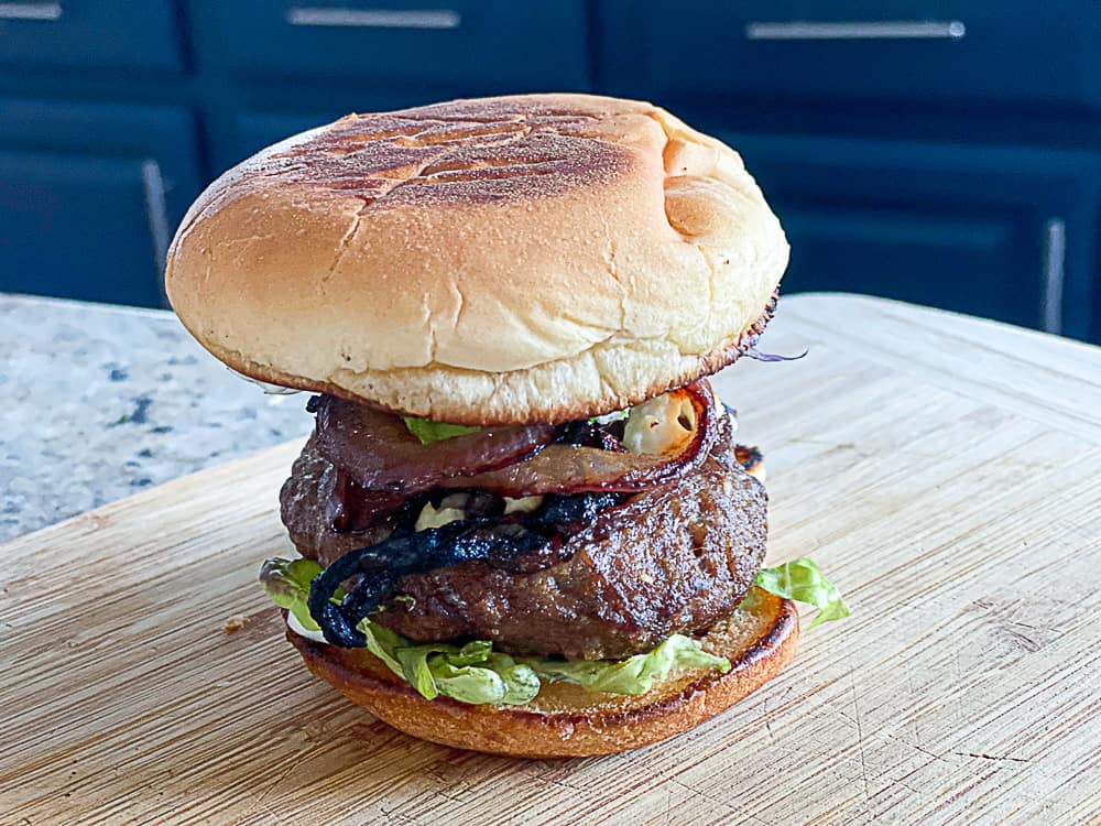 Side shot of sous vide lamb burger with toasted bun on a cutting board.