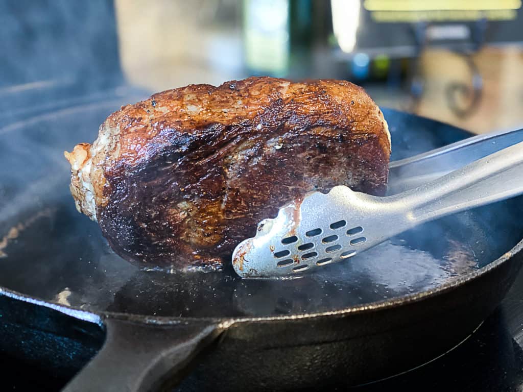 Closeup of ribeye steak purchased online being seared in a cast iron pan.