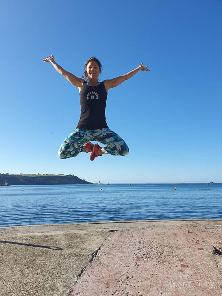 woman jumping in the air in front of a body of water