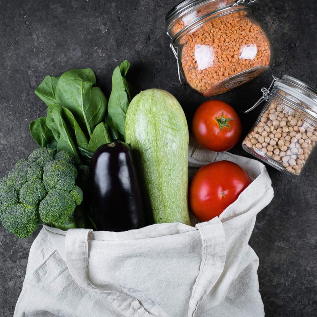 vegetables coming out of a canvas bag with beans in glass jars