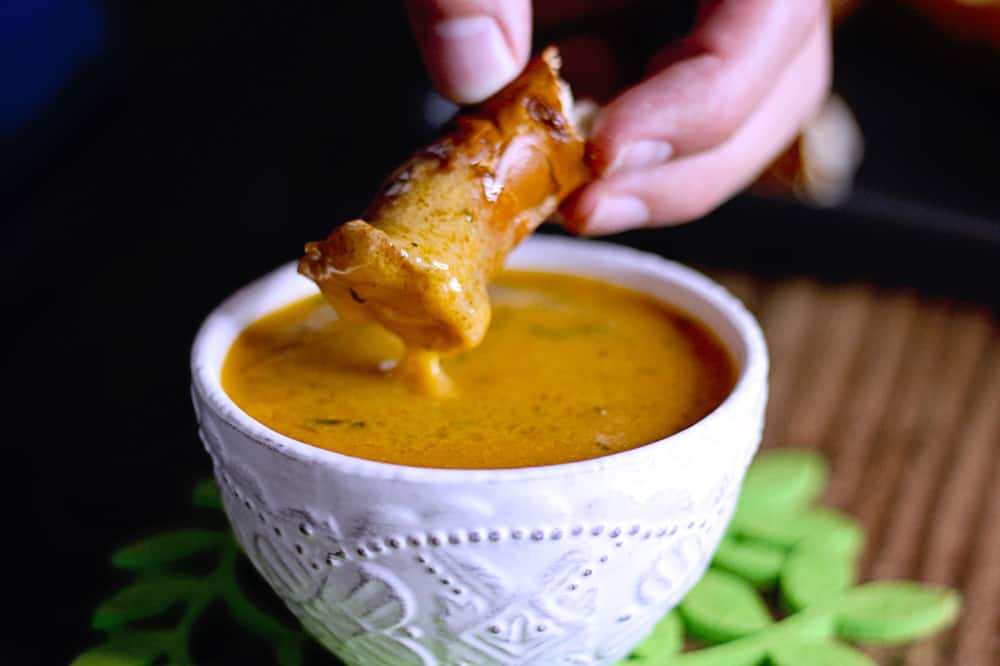 Side shot of hands dipping pretzel in cheddar beer cheese dip in a bowl.