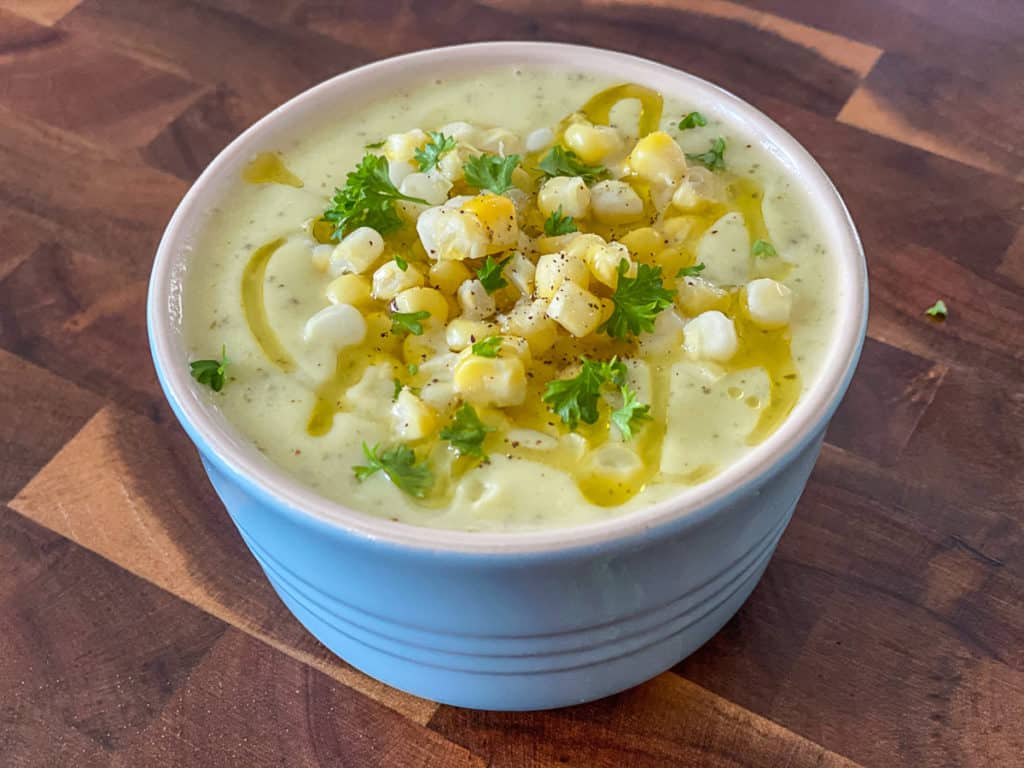 Side shot of corn topped zucchini soup in a bowl.