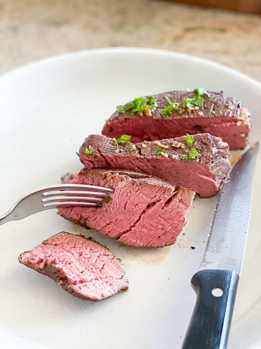 Sliced filet mignon steak on a white plate.