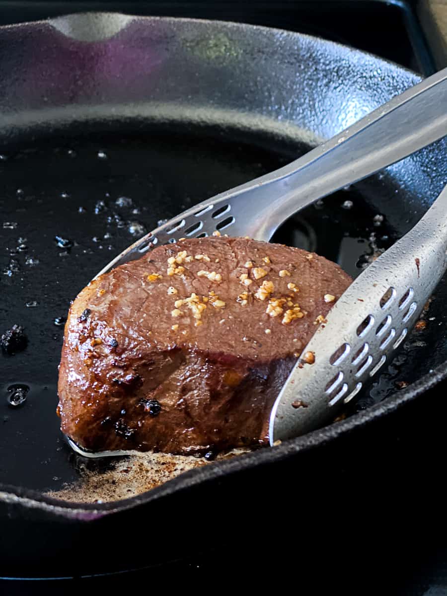 Filet mignon steak being seared in pan.