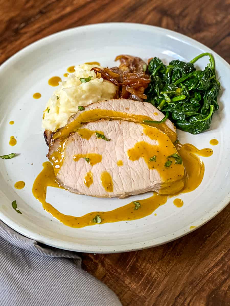 Side shot of honey mustard sous vide pork sauce on pork loin with spinach and mashed potatoes.