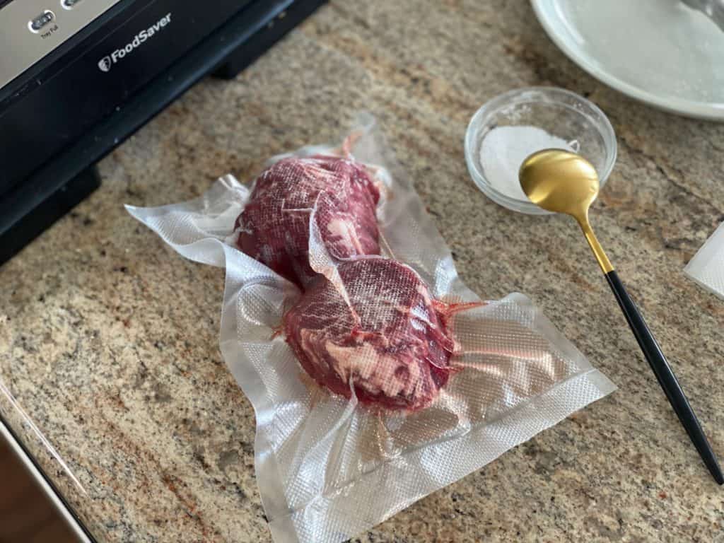 Top down shot of sous vide filet mignon with salt in a vacuum seal bag.