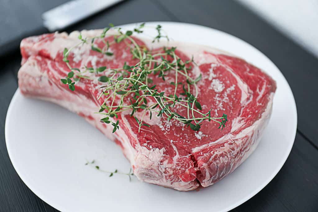 Side shot of Raw Prime rib with thyme on a plate.