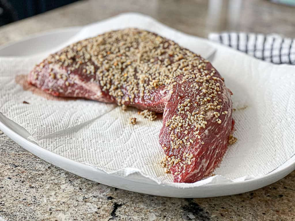 Side shot of Tri Tip Steak with garlic on a plate.