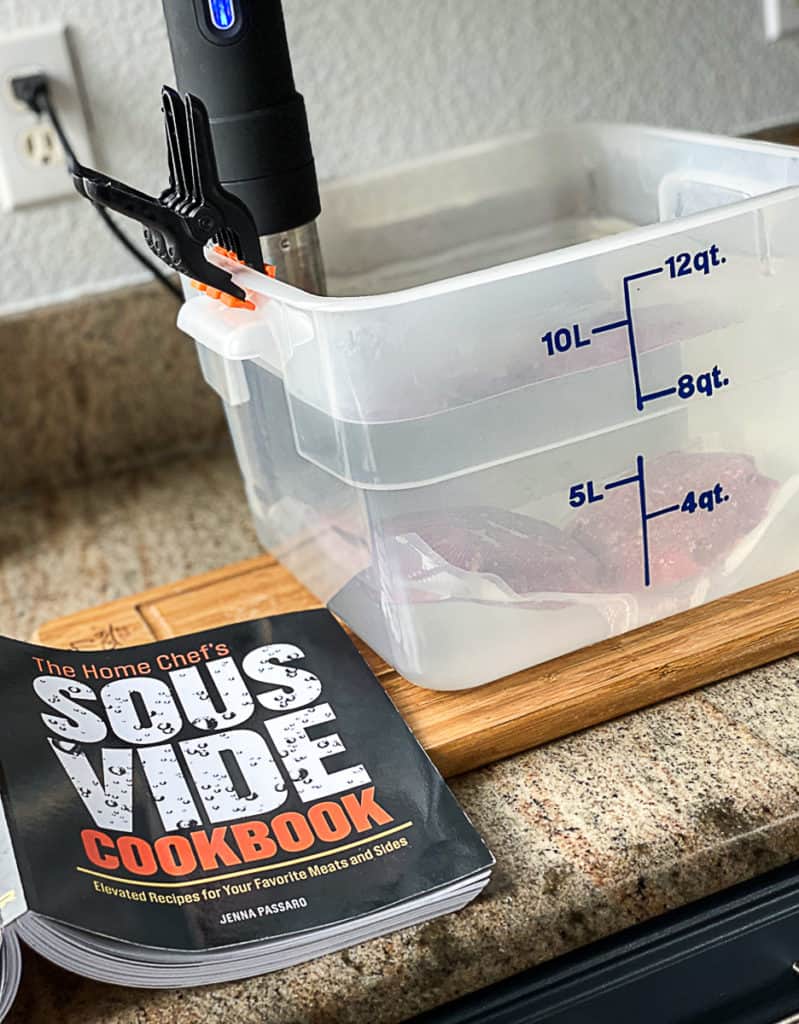 Side shot of the home chef's sous vide cookbook and sous vide food in water bath with anova machine.