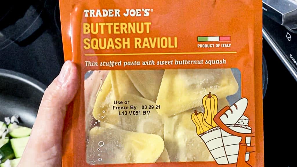 Top shot of hand holding a package of butternut squash ravioli from trader joe's brand.