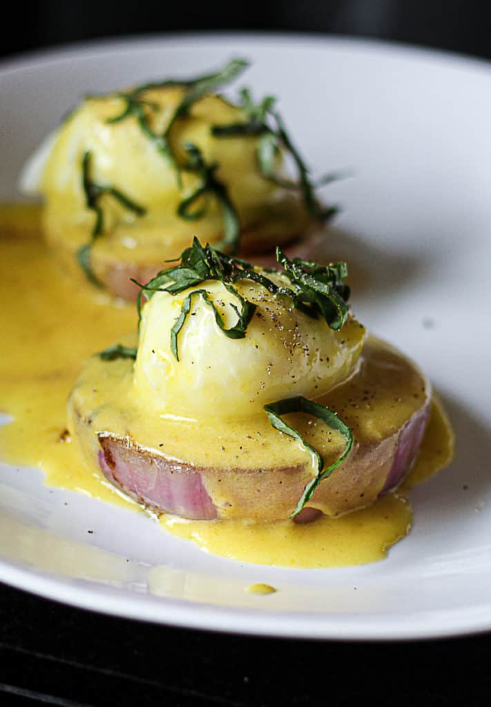 Closeup of sous vide poached eggs with hollandaise sauce on a plate with onion.