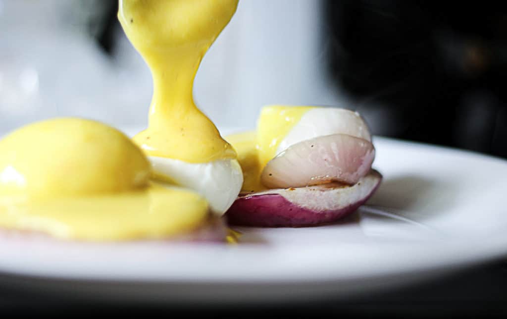 Drizzling hollandaise sauce on poached sous vide eggs.