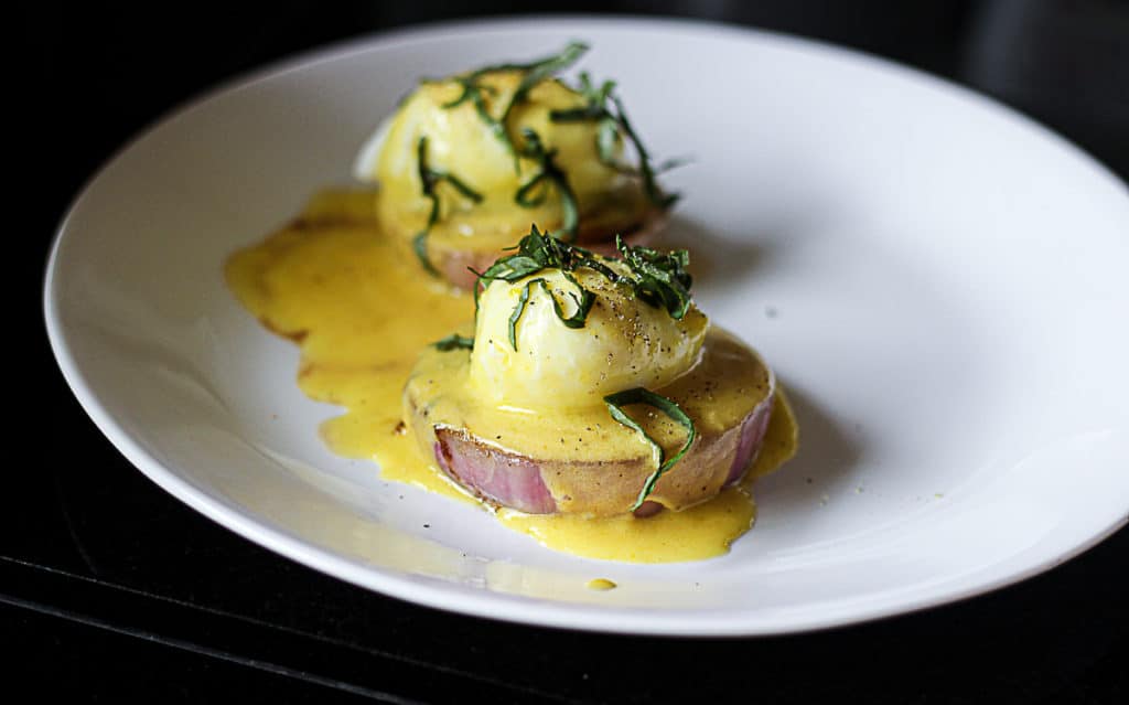 Side shot of sous vide eggs with hollandaise sauce on a plate.