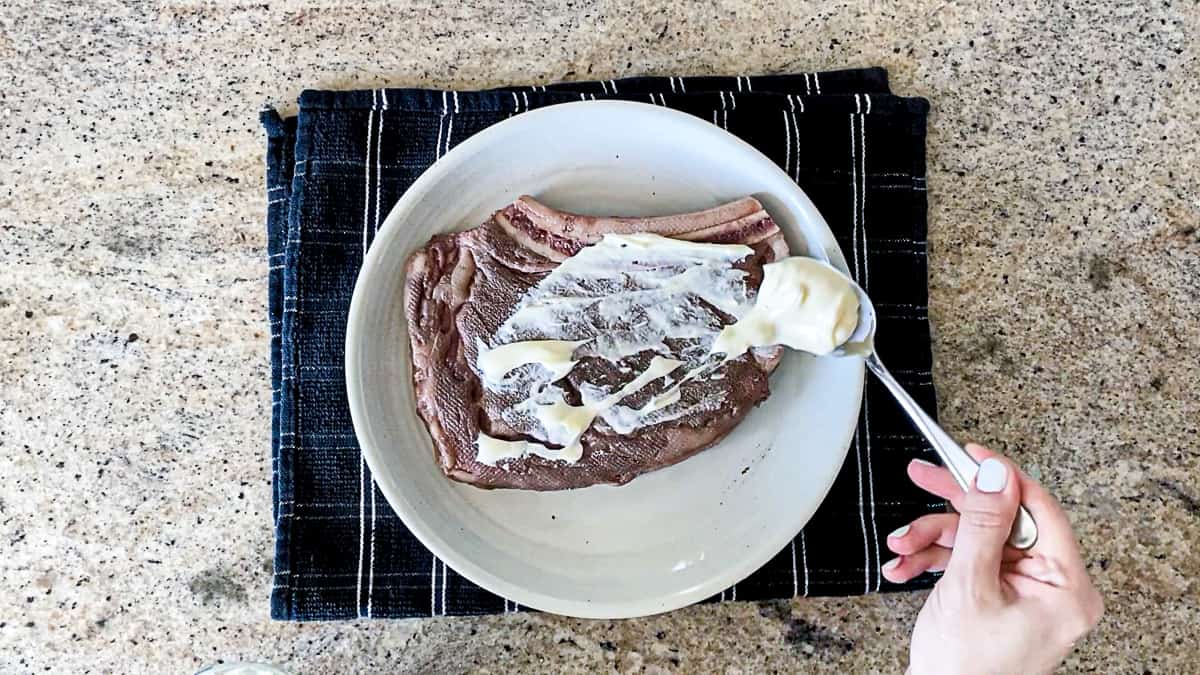 Top down shot of hand and spoon adding mayo to sous vide steak.