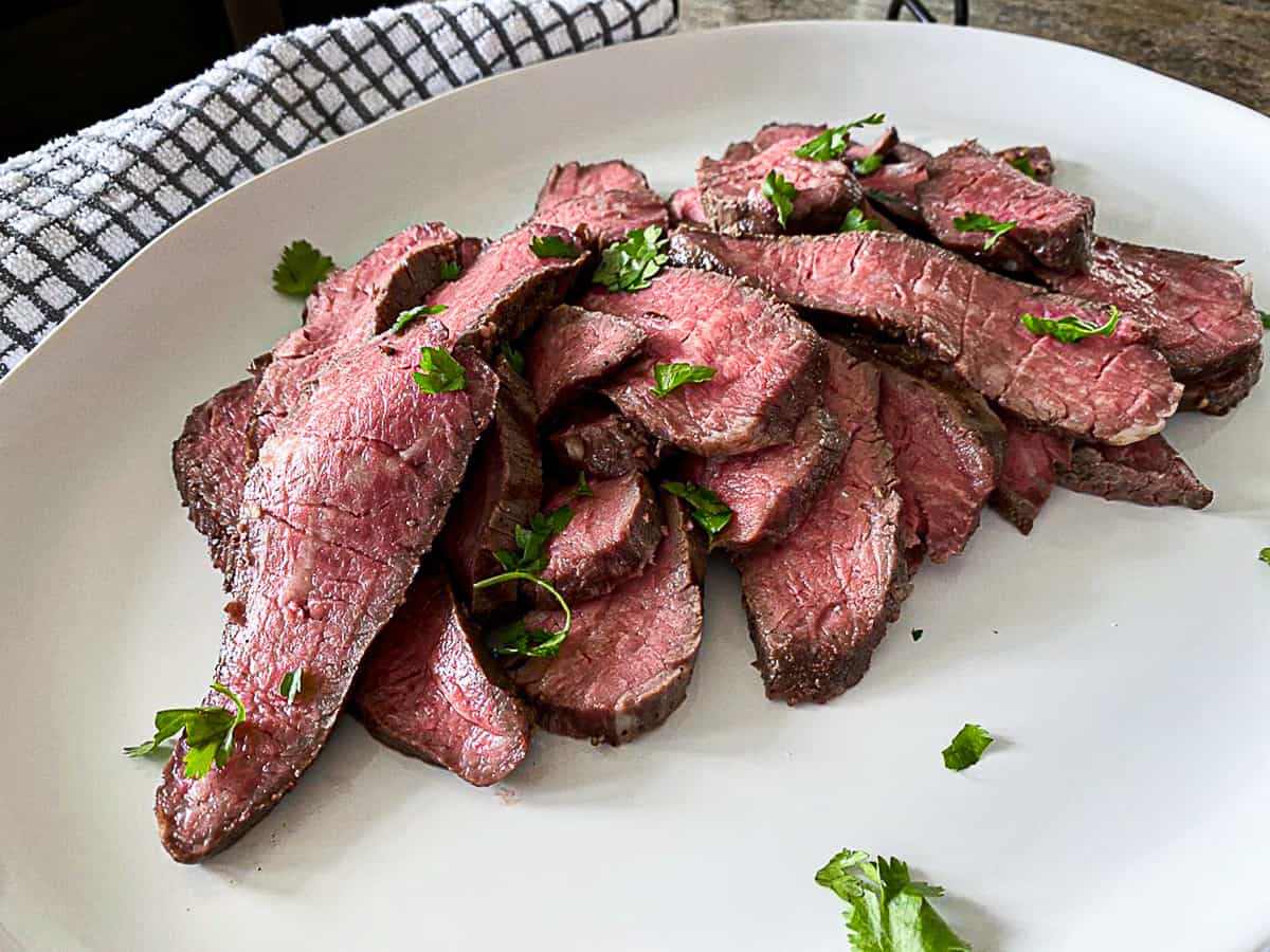 Side shot of simple herb seasoning on sous vide tri tip steak sliced on a plate.