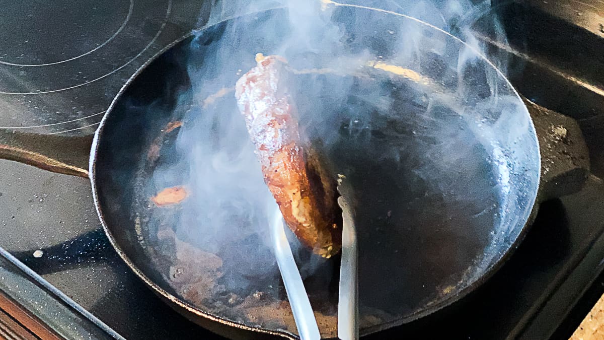 Top down shot of searing sous vide steak in cast iron skillet with finishing seasonings and butter