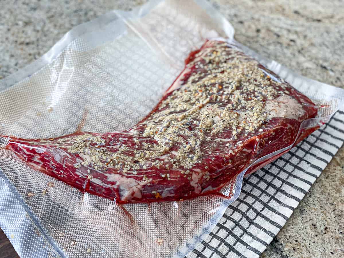 Side shot of seasoned steak in a vacuum seal bag with garlic and spices.